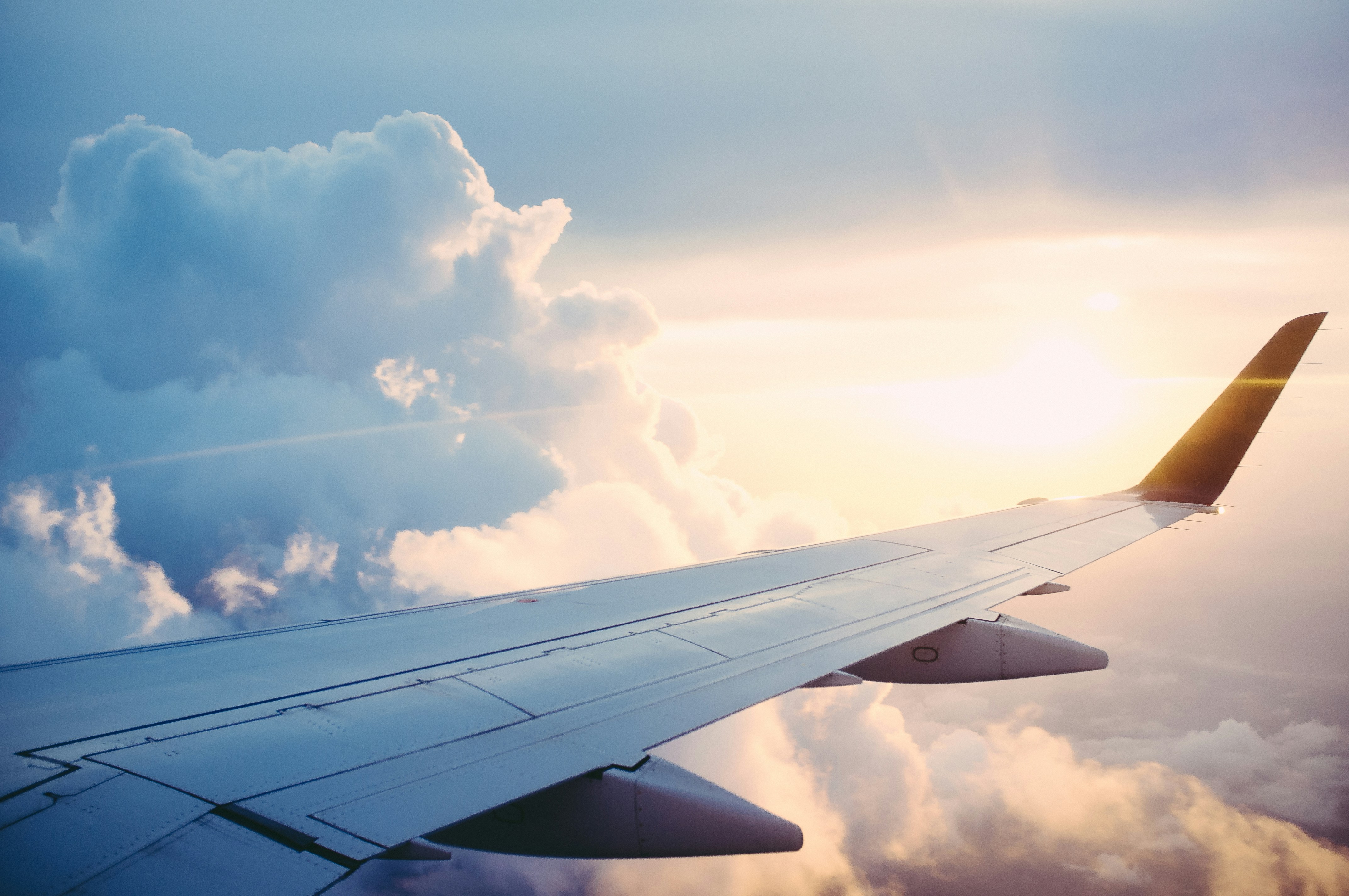 Wing of a plane in the light blue sky with white clouds all around